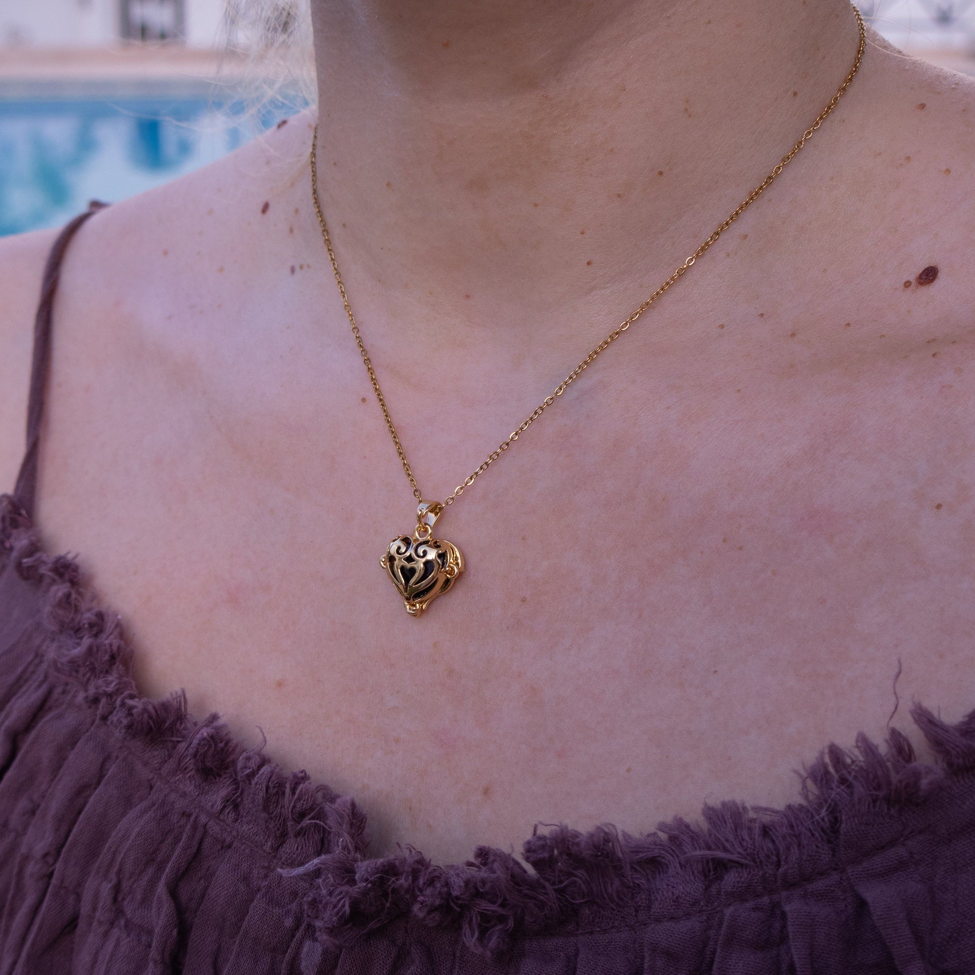 Gold necklace with a heart pendant worn by a person in a purple top, with a blurred background.