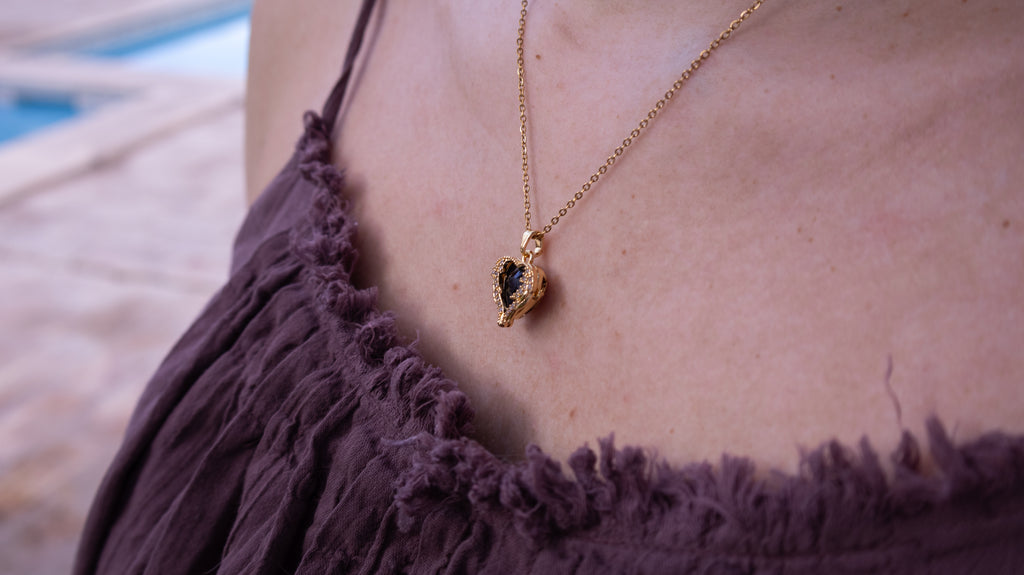 Gold necklace with a pendant on a person wearing a purple top, blurred background