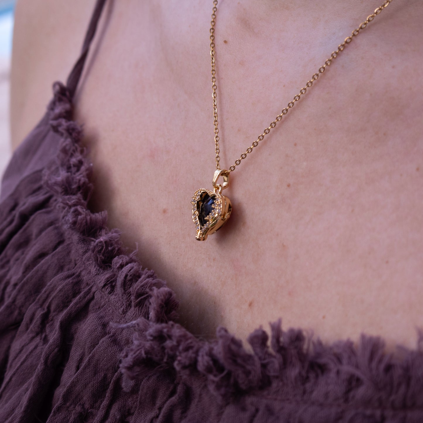 Gold necklace with a pendant on a person wearing a purple top, blurred background