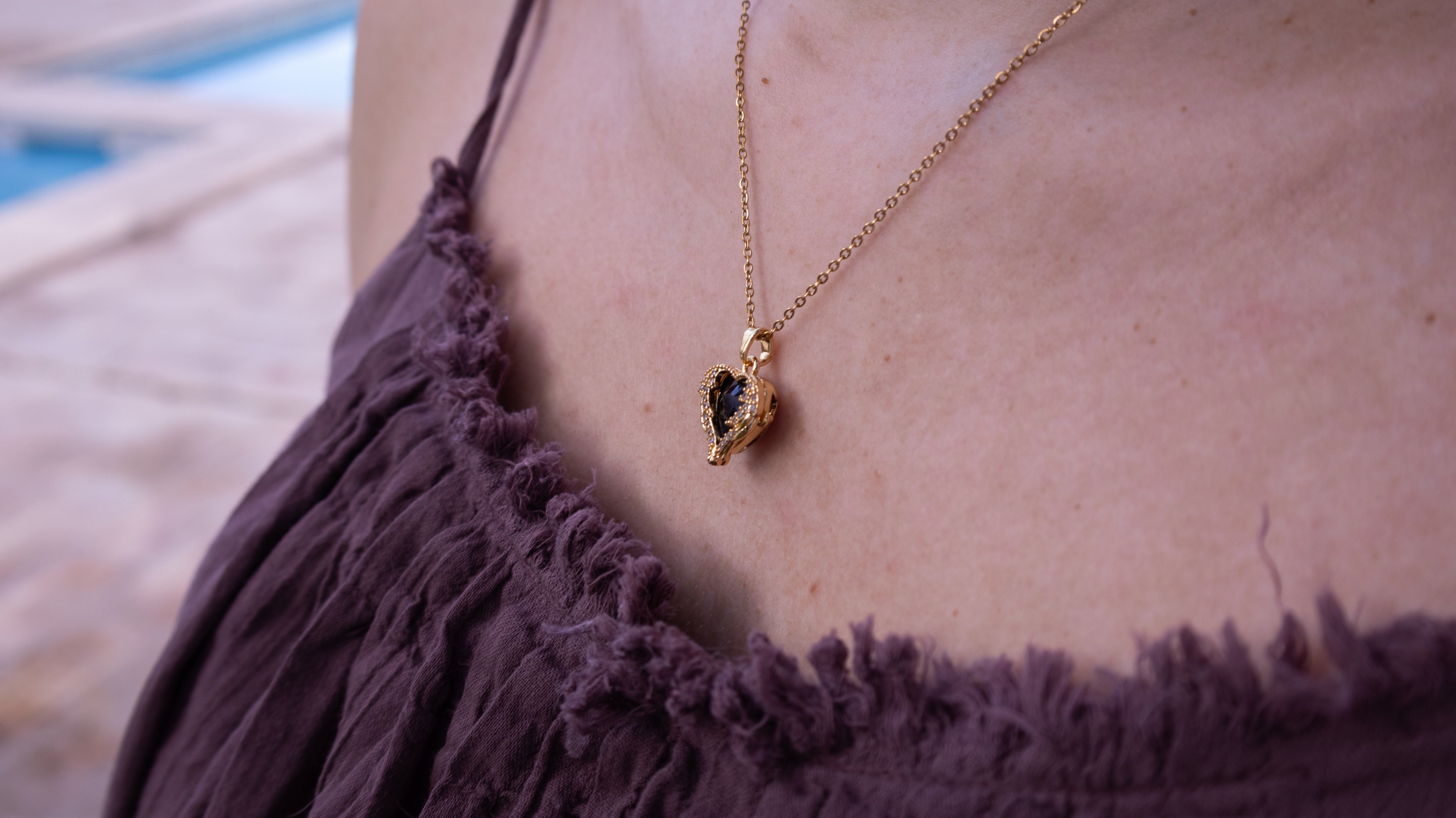 Gold necklace with a pendant on a person wearing a purple top, blurred background