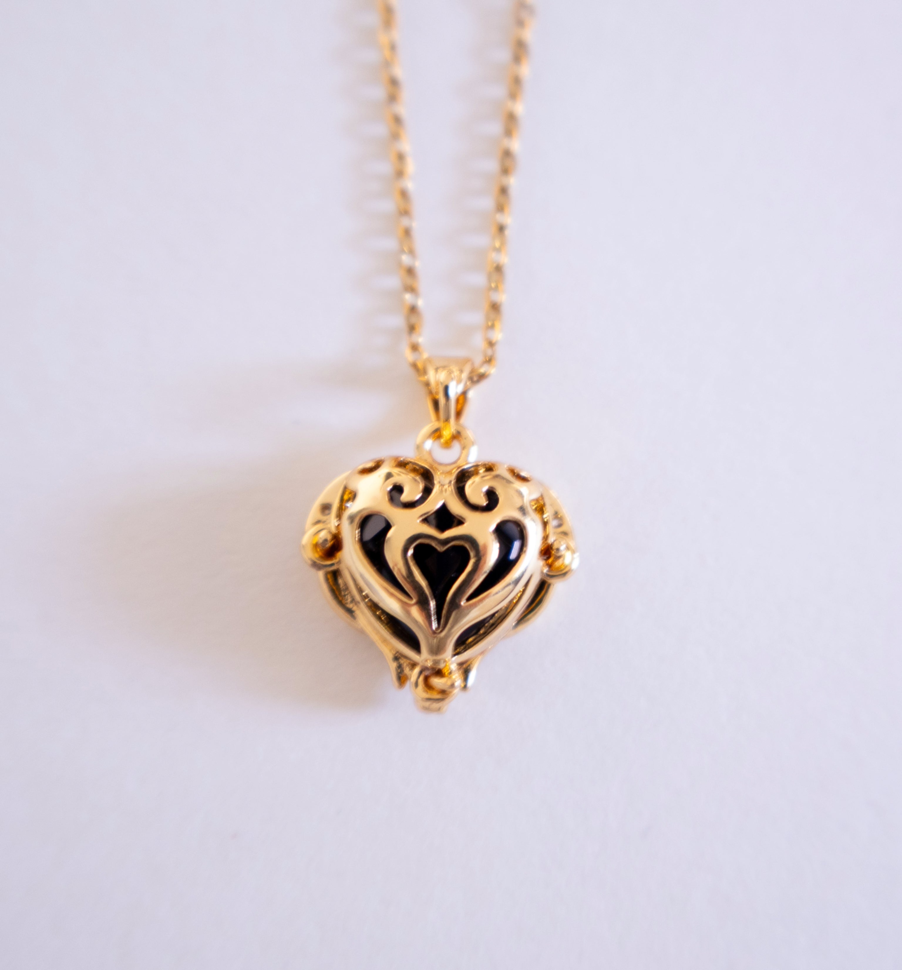Gold heart-shaped necklace with black interior on a light gray background