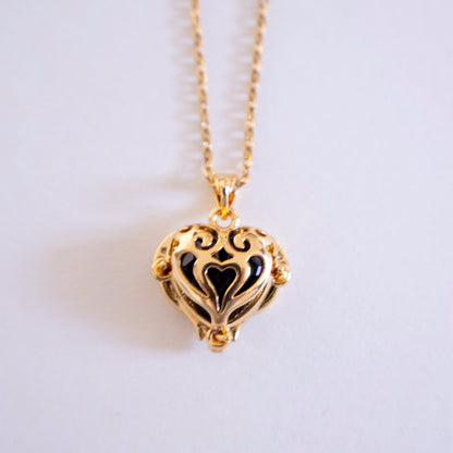 Gold heart-shaped necklace with black interior on a light gray background