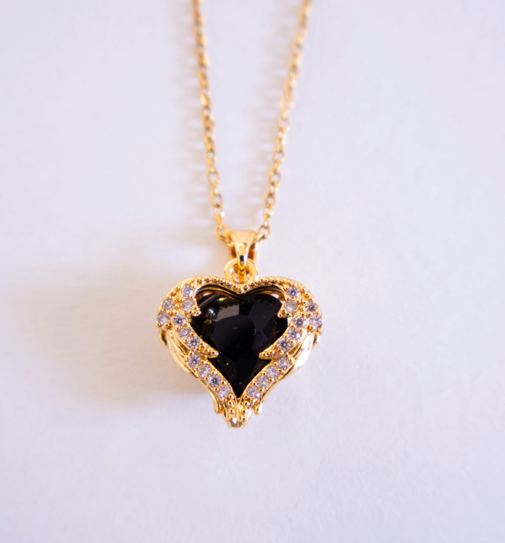 Gold necklace with a heart-shaped pendant featuring a black gemstone on a light gray background