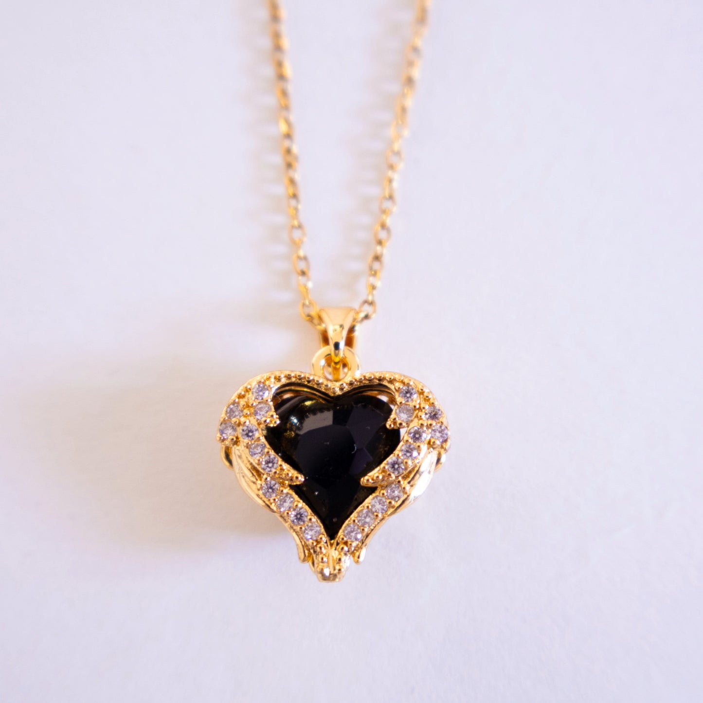 Gold necklace with a heart-shaped pendant featuring a black gemstone on a light gray background