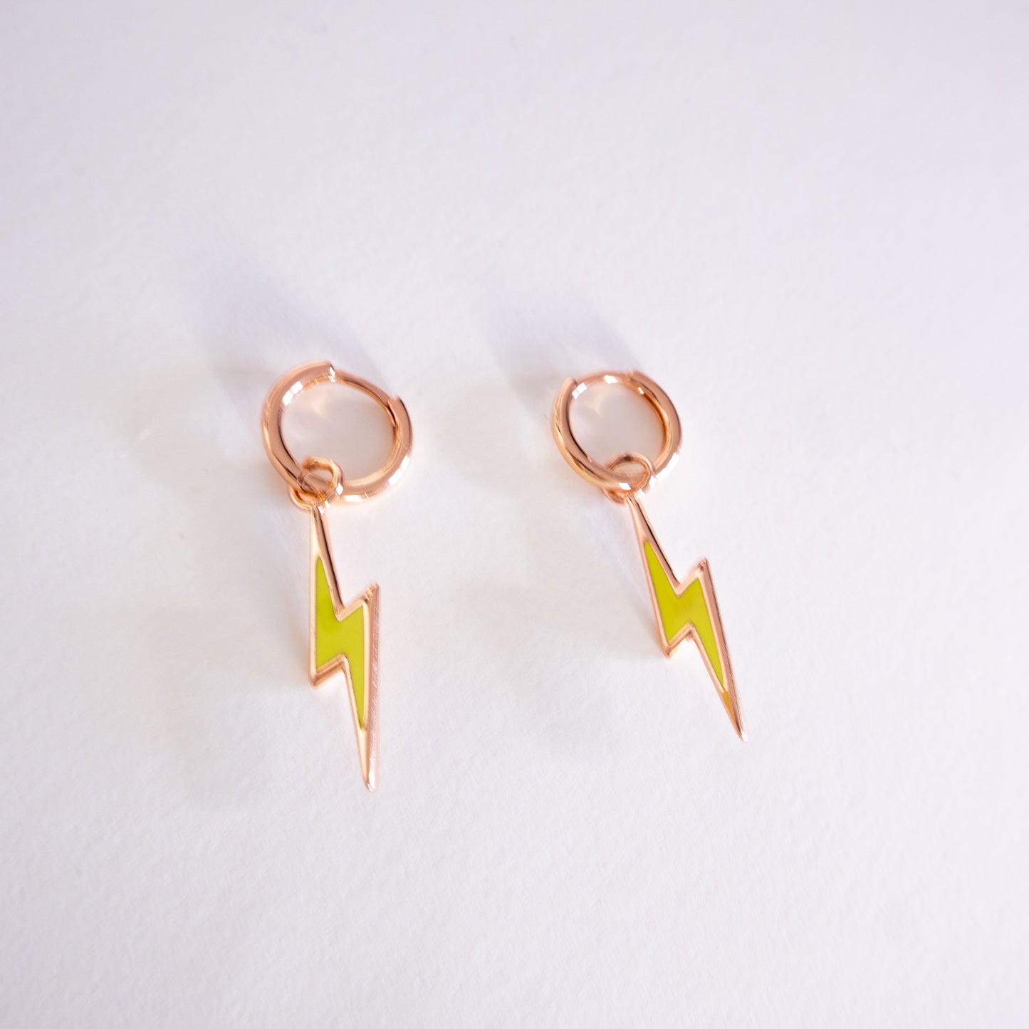 Rose gold earrings with green lightning bolt designs on a light gray background