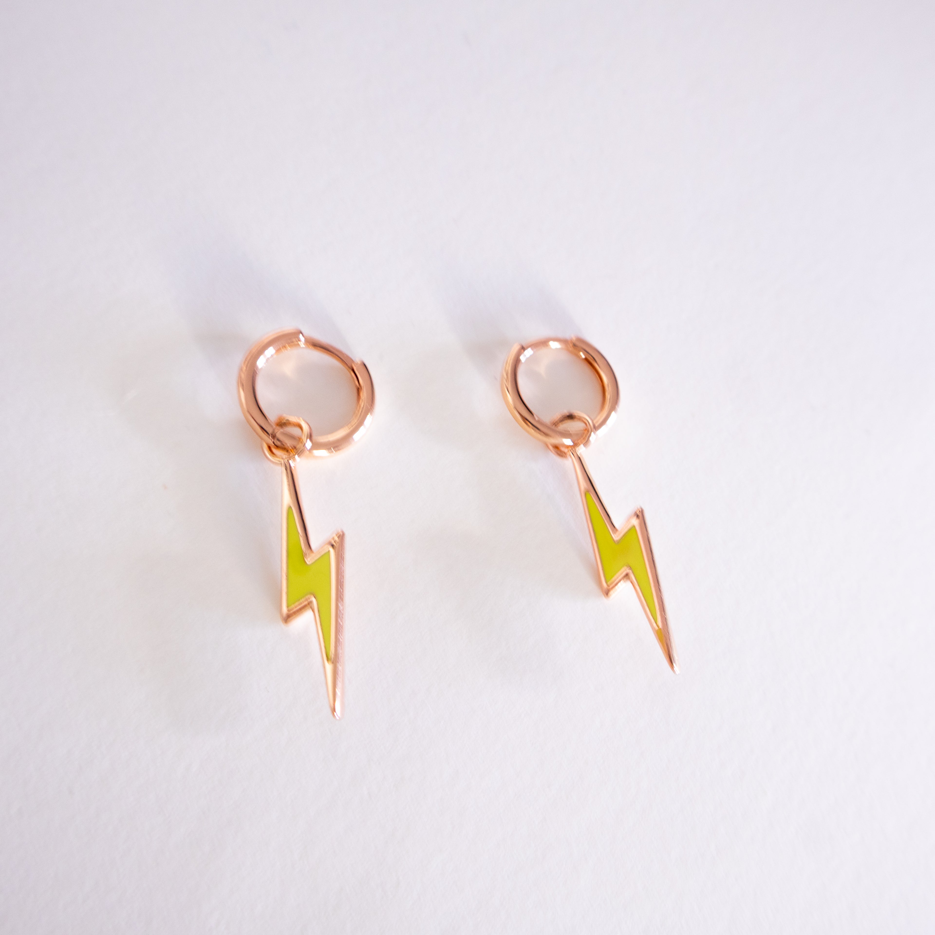 Rose gold earrings with green lightning bolt designs on a light gray background