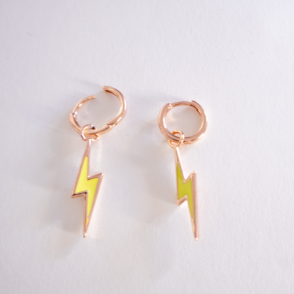 Pair of rose gold hoop earrings with yellow lightning bolt charms on a light gray background