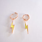Pair of rose gold hoop earrings with yellow lightning bolt charms on a light gray background