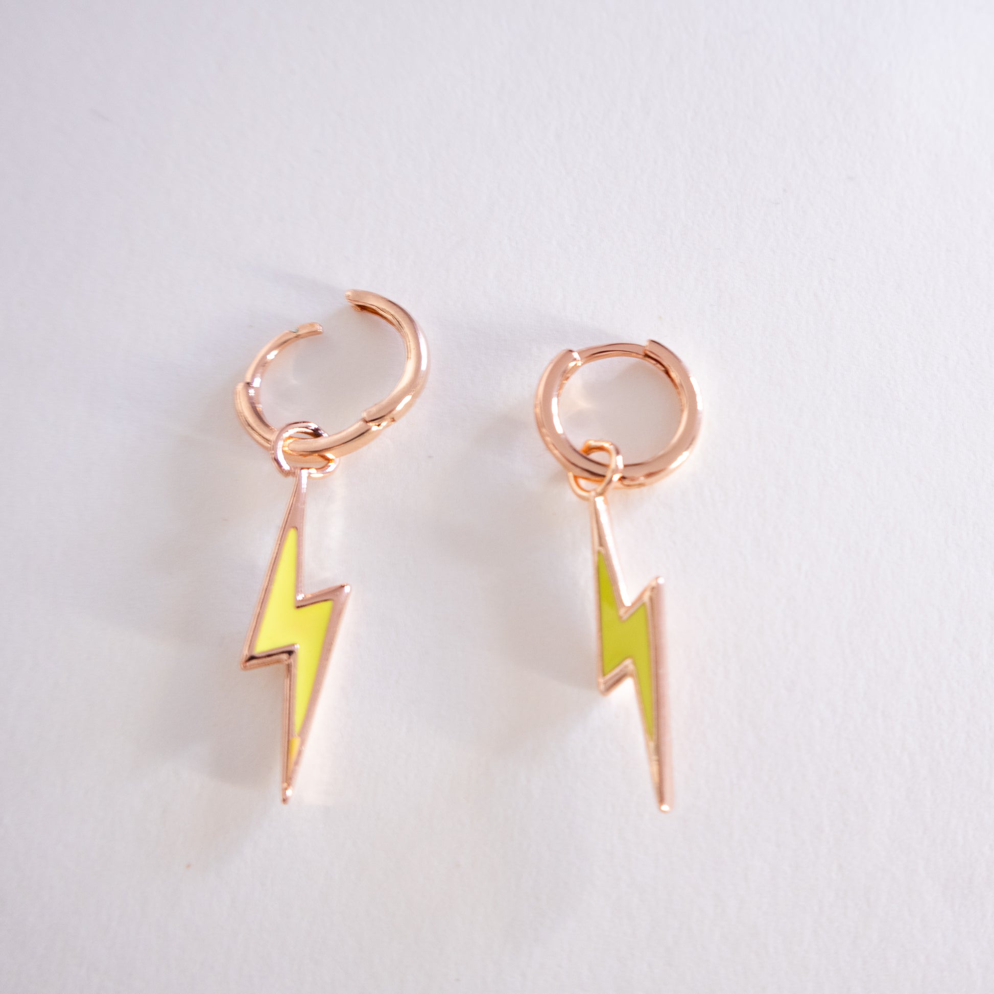 Pair of rose gold hoop earrings with yellow lightning bolt charms on a light gray background