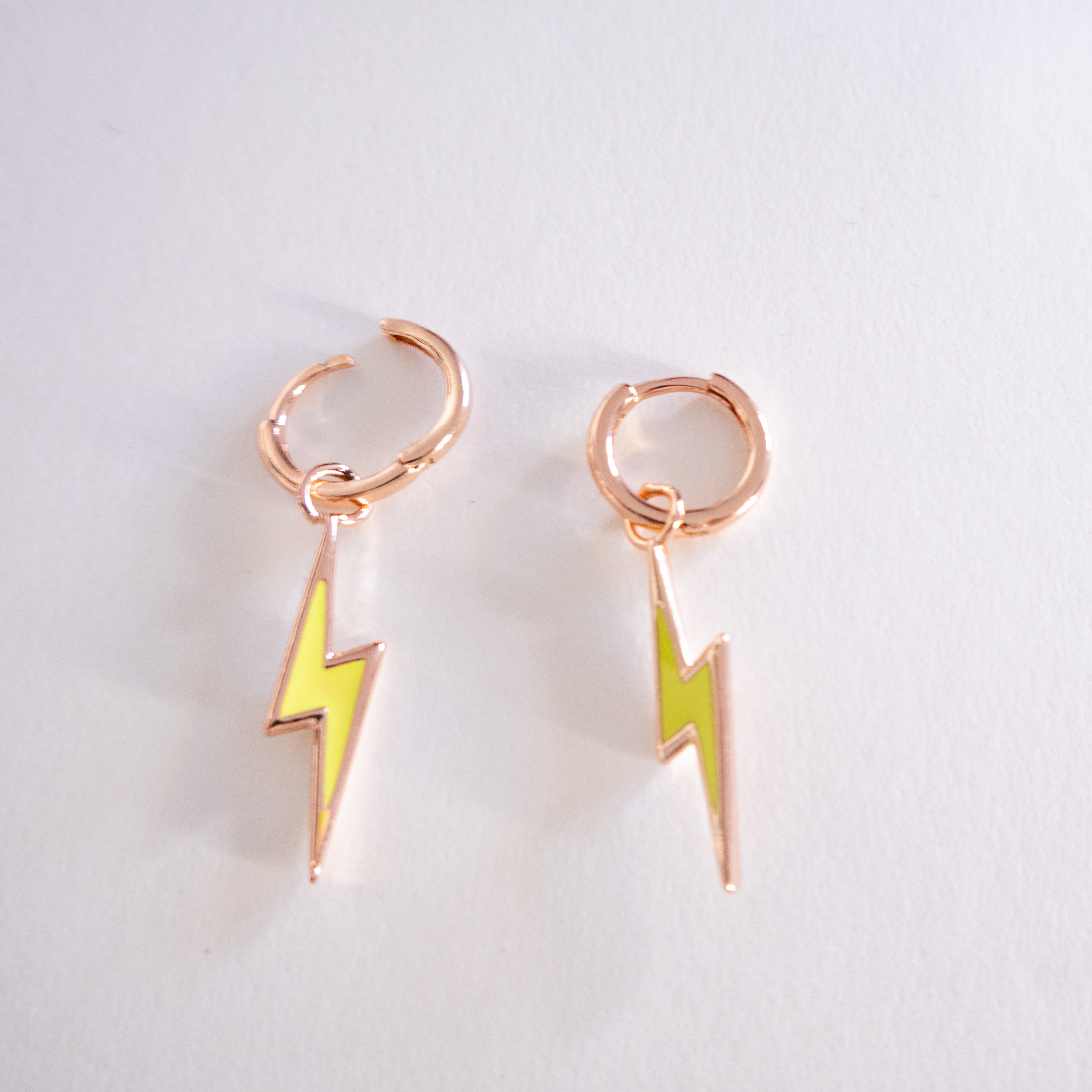 Pair of rose gold hoop earrings with yellow lightning bolt charms on a light gray background