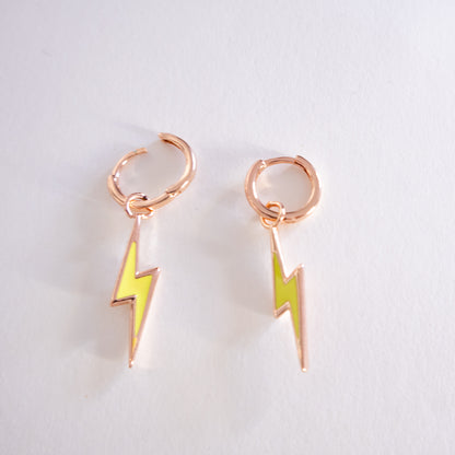 Pair of rose gold hoop earrings with yellow lightning bolt charms on a light gray background