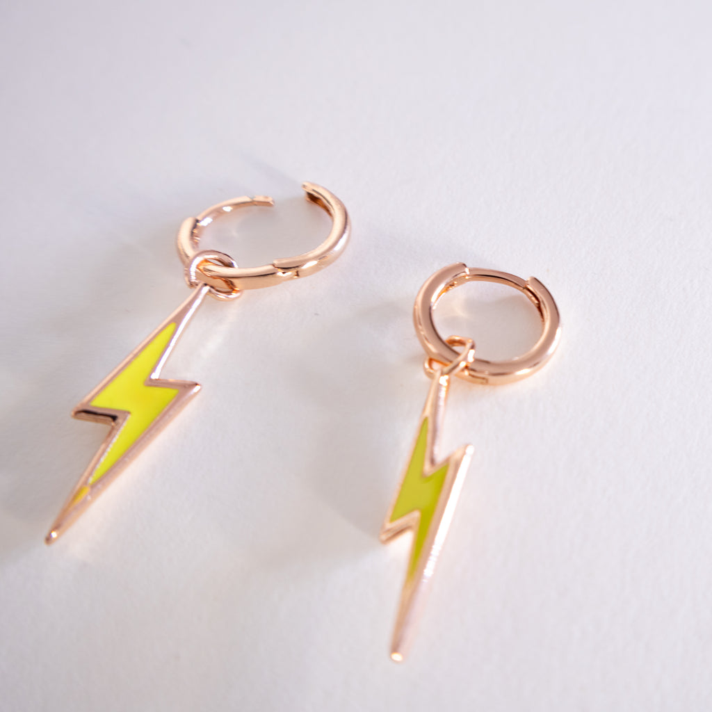 Pair of earrings with rose gold loops and green lightning bolt charms on a light gray background