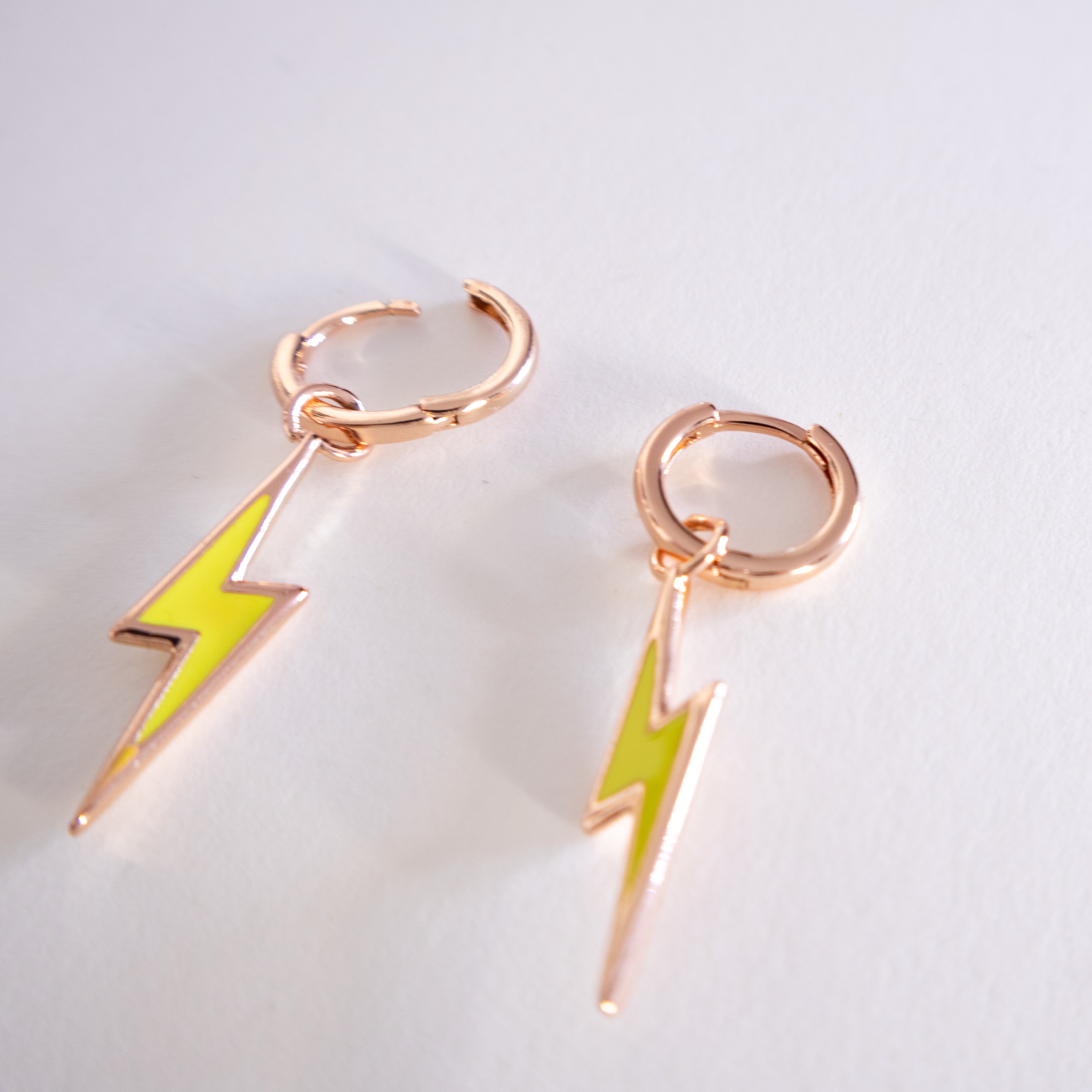 Pair of earrings with rose gold loops and green lightning bolt charms on a light gray background