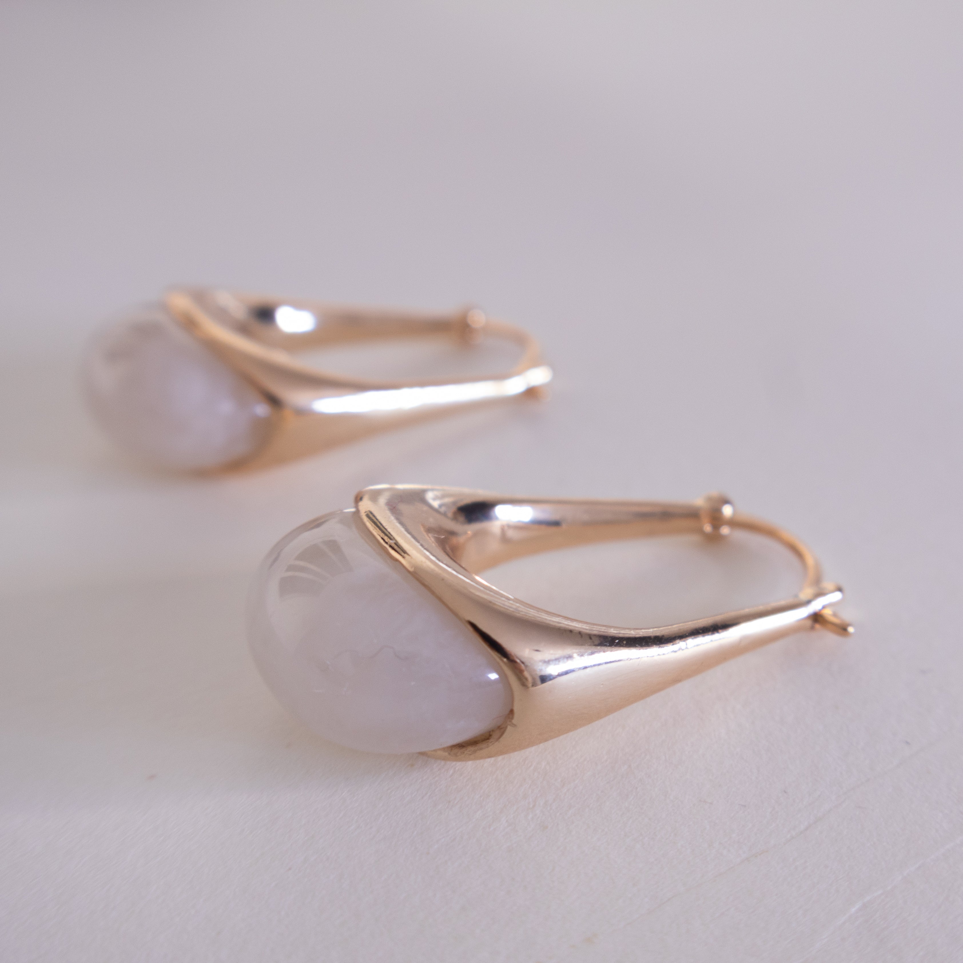 Gold hoop earrings with a light stone on a white background