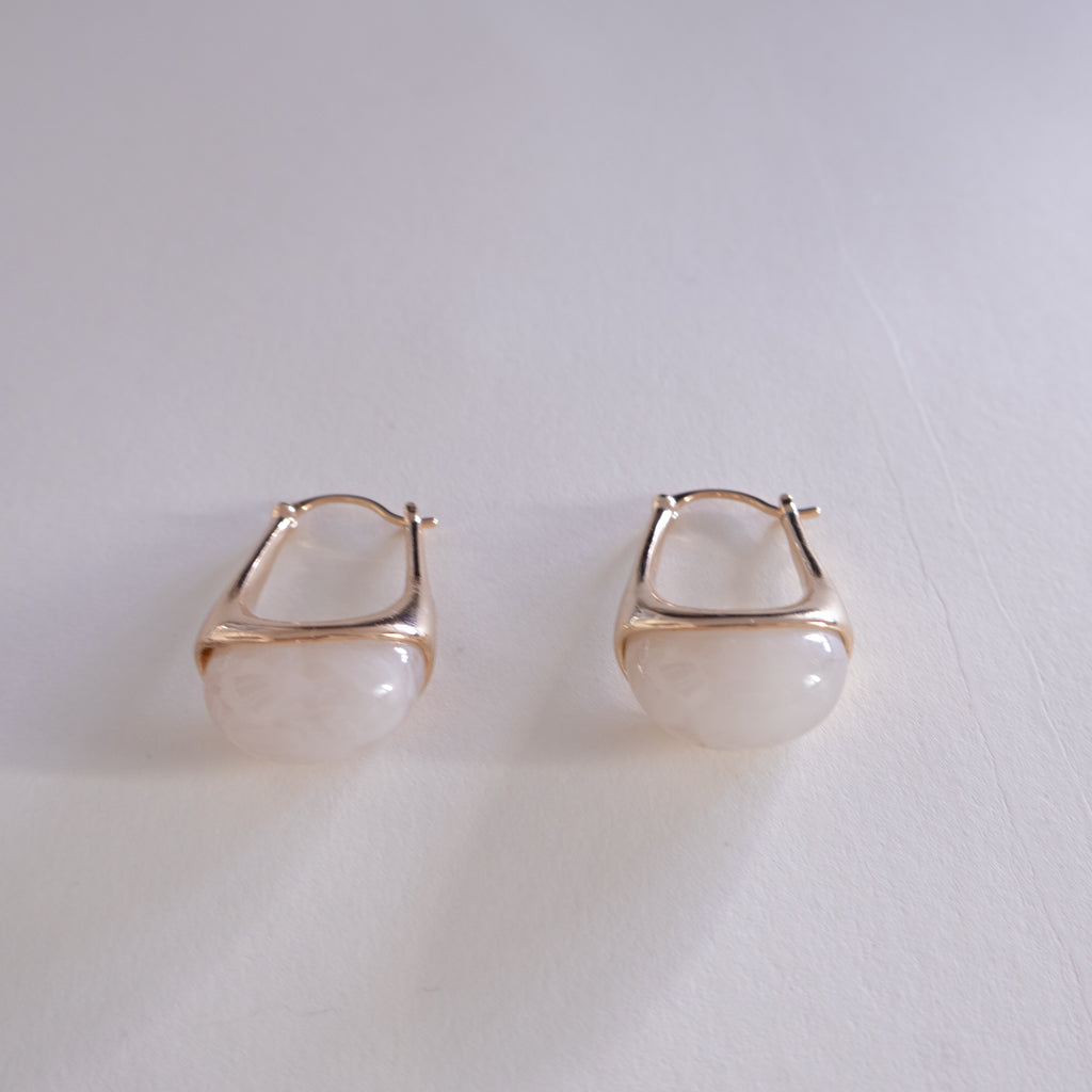 Pair of gold hoop earrings with a white stone on a light gray background