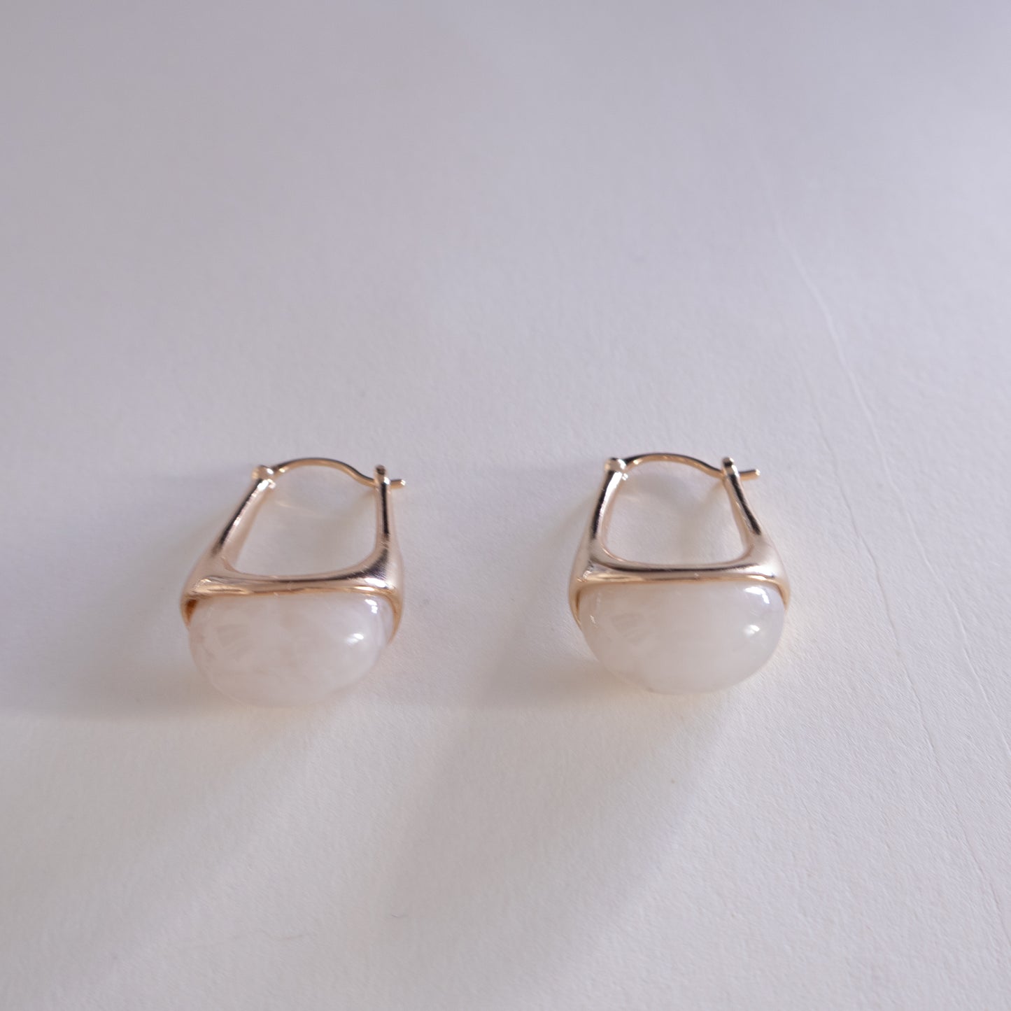 Pair of gold hoop earrings with a white stone on a light gray background