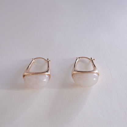 Pair of gold hoop earrings with a white stone on a light gray background