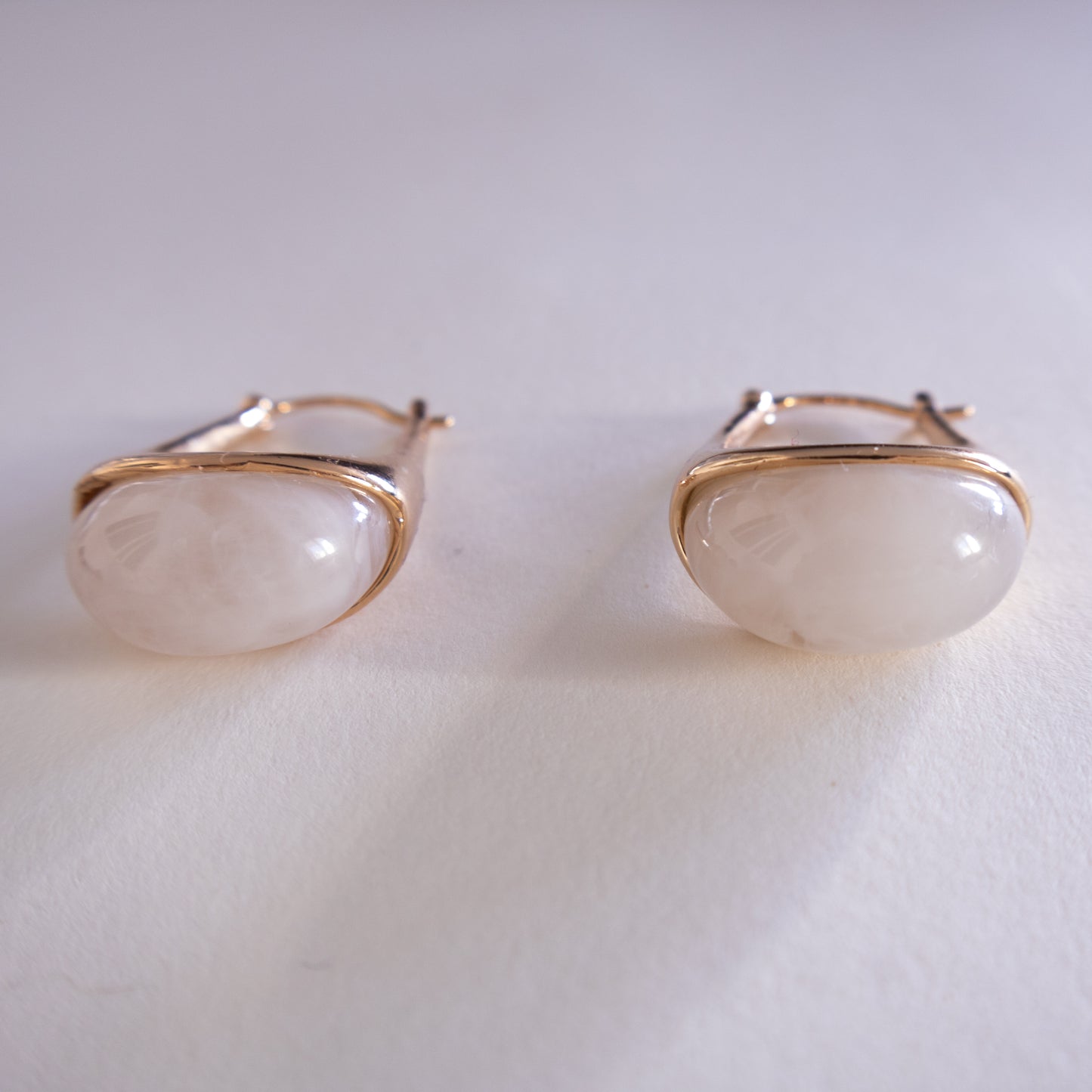 Pair of gold earrings with white stones on a light gray background