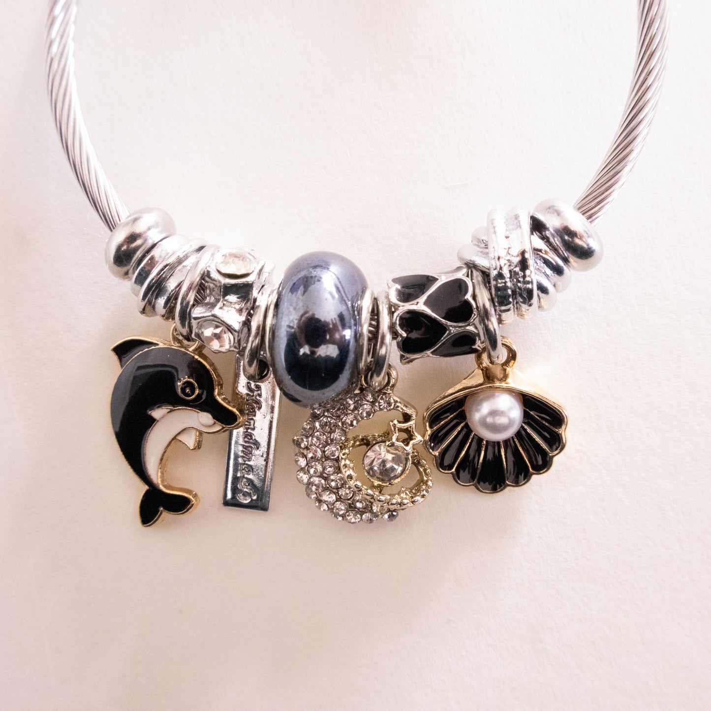 bracalet with various charms including a dolphin, shell, and pearl on a light background